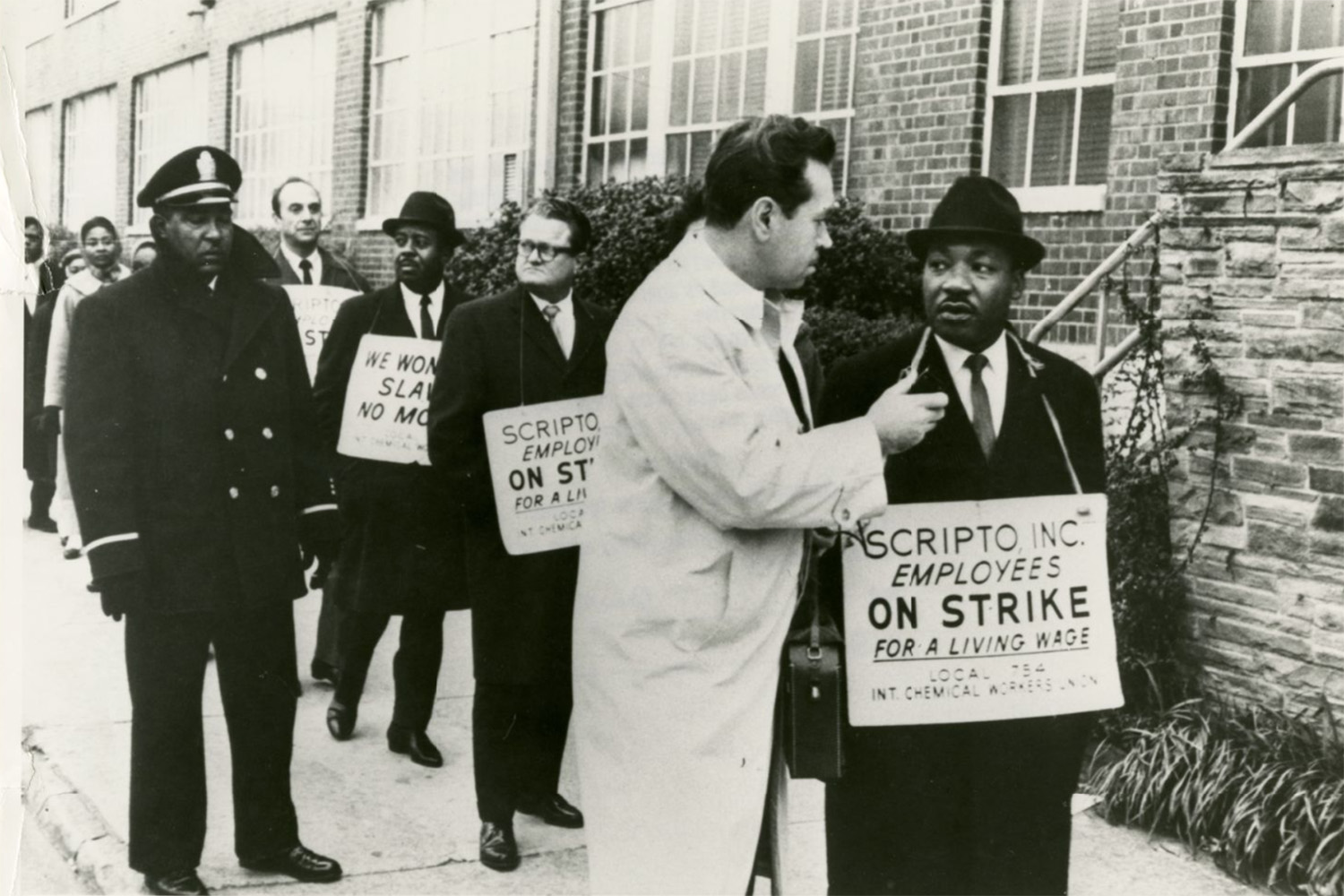 a white man approaches. Dr. Martin Luther King Jr. as he marches with employees of Scripto Inc. on a picket line wearing signs