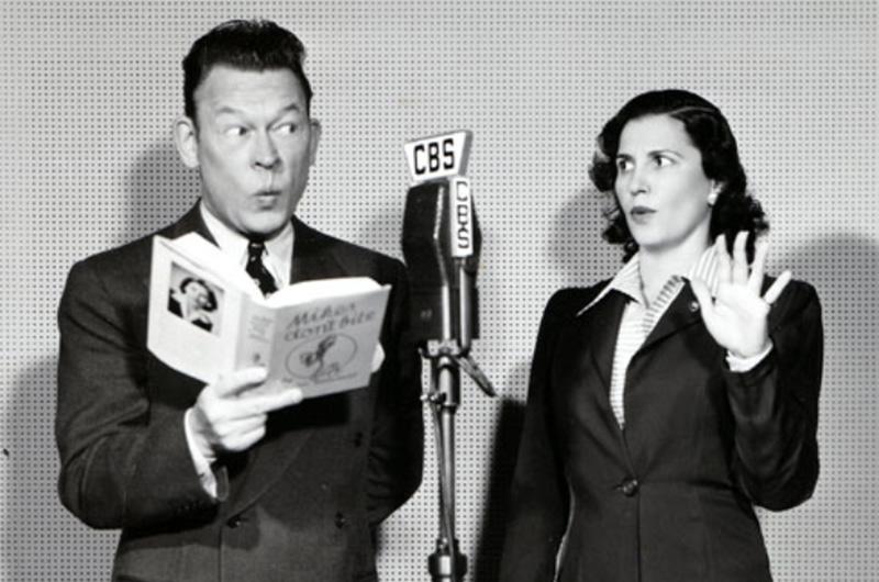 A man and woman stand near a microphone, making dramatic faces